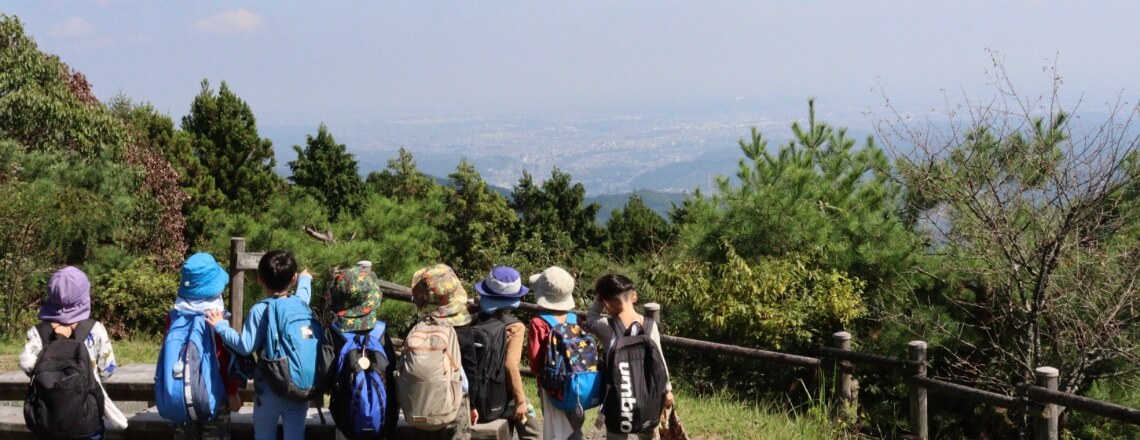 写真：山の山頂付近で園児たちが並んで遠くの景色を見渡す様子