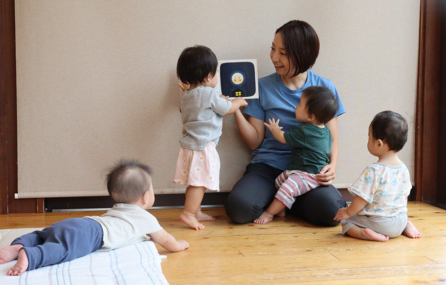 写真：子どもにミルクをあげる先生とそれを見守る子どもたち