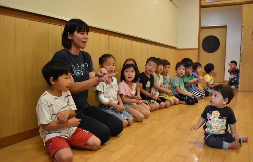 写真：保育士が両手で生き物の形を作り、園児たちがそれが何かを考えて楽しむ様子