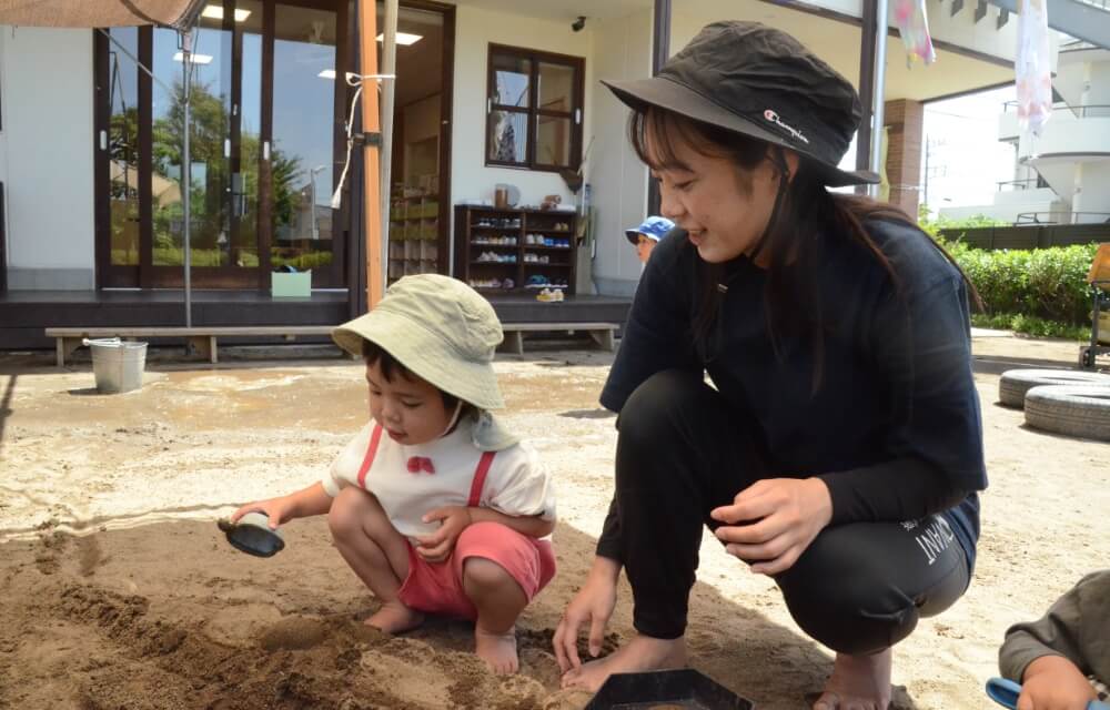 写真：保育士と園児が砂場遊びを楽しむ様子