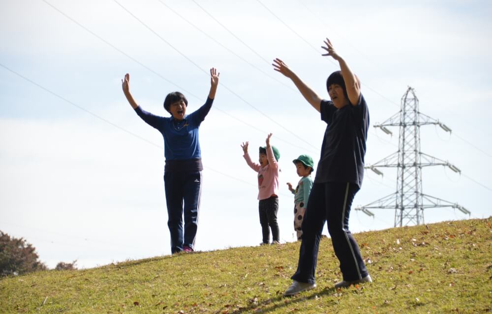 写真：丘の上で先生と子どもたちが手のジェスチャーを使ってコミュニケーションを取り合う様子