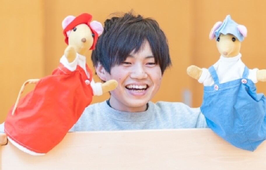 写真：両手に手人形をはめて笑顔を見せる男性の先生